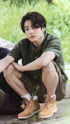 a young man sitting on the ground with his legs crossed, wearing brown shoes and green shirt