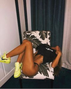 a woman laying on top of a chair with her legs crossed and yellow shoes in front of her