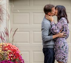 a man and woman kissing in front of a garage with flowers on the ground behind them