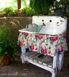 an old fashioned sink in the middle of a garden with flowers and potted plants