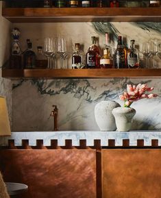 a marble bar with bottles and glasses on the top shelf, along with a vase filled with flowers