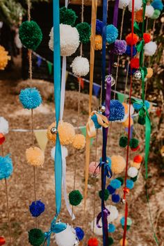 many colorful pom poms hanging from the side of a tree with ribbons attached to them