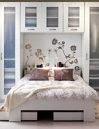 a white bed sitting in a bedroom next to a tall cabinet with flowers on it