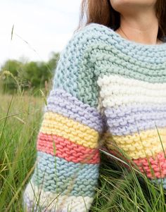 a woman is sitting in the grass wearing a colorful sweater