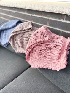 three crocheted blankets sitting on top of a gray couch next to a brick wall