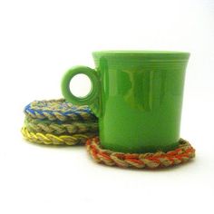 two green coffee mugs sitting next to each other on top of roped coasters