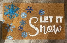 a door mat with the words let it snow written on it and blue snowflakes