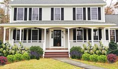 a white house with black shutters on the front porch and landscaping in front of it