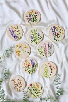 nine pressed flowers are arranged in the shape of circles on a white sheet with green leaves