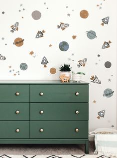 a green dresser sitting in front of a wall with space decals on it