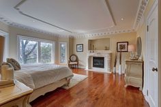 a large bedroom with hardwood floors and white furniture in front of a fireplace on the wall