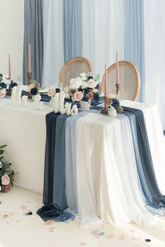 the table is set up with blue and white linens, candles, and flowers