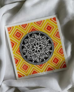 an orange and yellow patterned paper with a black design on it, laying on a white sheet