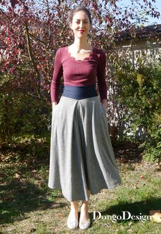 a woman standing in front of a tree wearing a red top and grey midi skirt