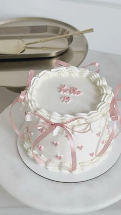 a white cake with pink ribbon and bow on the top is sitting on a plate