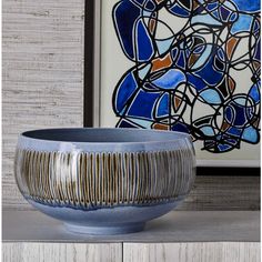 a blue bowl sitting on top of a wooden table next to a framed art piece