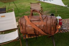 a brown duffel bag sitting on top of a wooden picnic table next to chairs