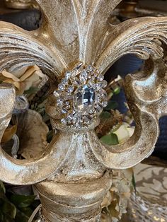 an ornately decorated gold candle holder with crystal stones on the top and sides, surrounded by flowers