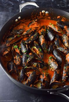 a pan filled with mussels and sauce on top of a table