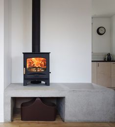 a wood burning stove sitting on top of a cement bench next to a wall with a clock above it