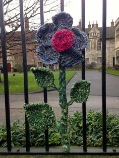 a crocheted flower sitting on top of a metal fence in front of a building