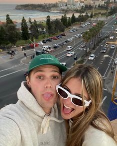 a man and woman taking a selfie in front of a busy street with cars