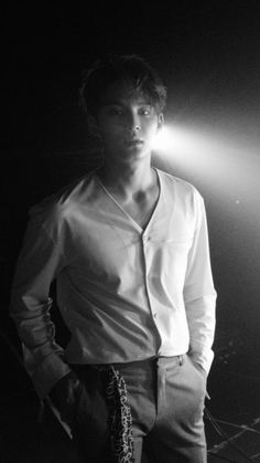 a man standing in the dark with his hands on his hips wearing pants and a white shirt