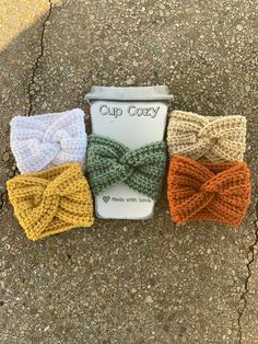 three crocheted bows are sitting on the ground next to a cup that says cup cozy