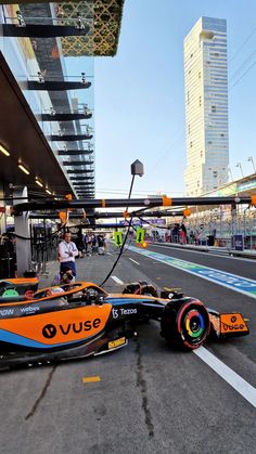 an orange and blue race car is on the ground in front of some tall buildings