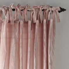 pink curtains hanging on the side of a white wall with black metal rod ends and tie backs