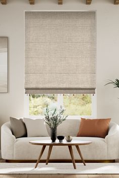 a white couch sitting under a window next to a table with flowers on it and a potted plant