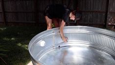 a woman bending over in an empty metal container on top of a wooden table outside