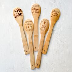 four wooden spoons with engraved names are lined up against a white wall, one has a heart and the other has an inscription on it