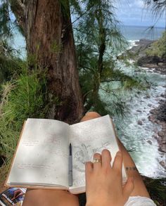 a person is reading a book by the water's edge with a pen in their hand