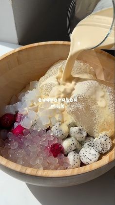 a wooden bowl filled with lots of ice cream and berries next to a bottle of milk