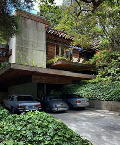 two cars are parked in front of a house with plants growing on the roof and balcony