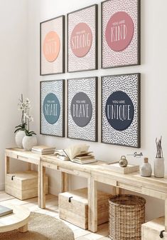 four framed art prints on the wall above a wooden table with baskets and vases