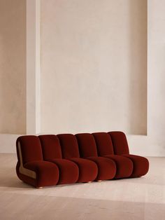 a red couch sitting on top of a hard wood floor next to a white wall