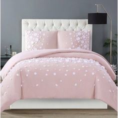 a pink comforter set with white flowers on it in front of a gray wall