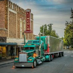 a green semi truck parked in front of a building on the side of the road