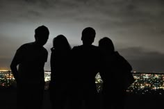 three people standing in front of a cityscape at night with their arms around each other