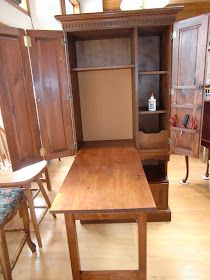 a wooden table sitting in the middle of a room next to chairs and cupboards