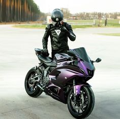 a person wearing a helmet and leather jacket standing next to a purple motorcycle on concrete