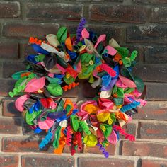 a multicolored wreath on the side of a brick wall with scissors attached to it