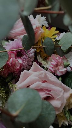 a bunch of flowers sitting on top of a table next to green leaves and branches