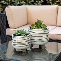 two white planters sitting on top of a glass table next to a beige couch