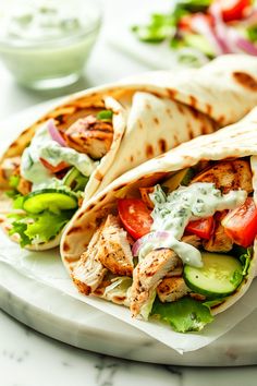 two pita sandwiches with chicken, cucumber and tomatoes on a white plate