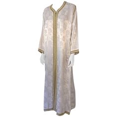 Elegant Moroccan caftan gown white embroidered with gold trim, circa 1970s. This long maxi dress kaftan is embroidered and embellished entirely by hand. One of a kind evening Moroccan Middle Eastern gown. The kaftan features a traditional neckline, with side slits and embellished sleeves in Moorish style. In Morocco, fashion preserves its traditional style inherited from great civilizations that found their way to Northwest Africa, such as the ottomans and the Moors. Moroccan fashion has been re Moroccan Fabric, Gown White, Maxi Kaftan, Dress Kaftan, Moroccan Kaftan, Moroccan Fashion, Emo Dresses, Moroccan Caftan, African Traditional Dresses