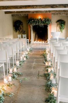 rows of white chairs are lined up with candles and greenery in front of the fireplace