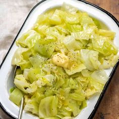 a white bowl filled with cabbage and some seasoning on top of the salad is sitting on a wooden table